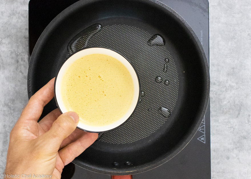 Adding chickpea socca flatbread batter to the frying pan to cook