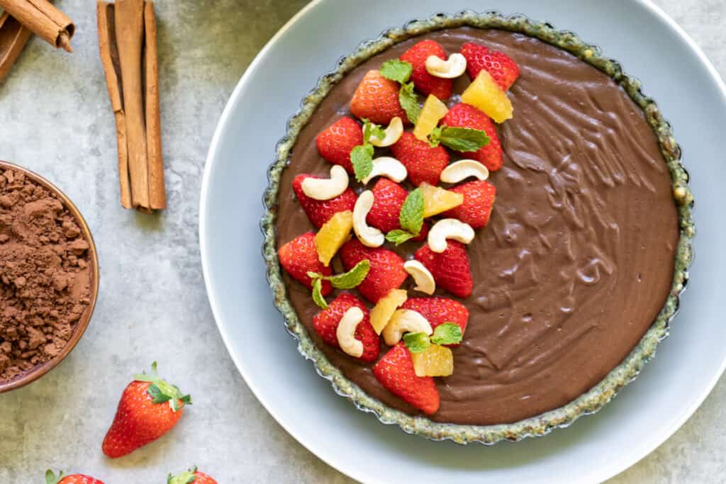 raw cheesecake garnished with fresh strawberries, orange, cashew and mint leaf