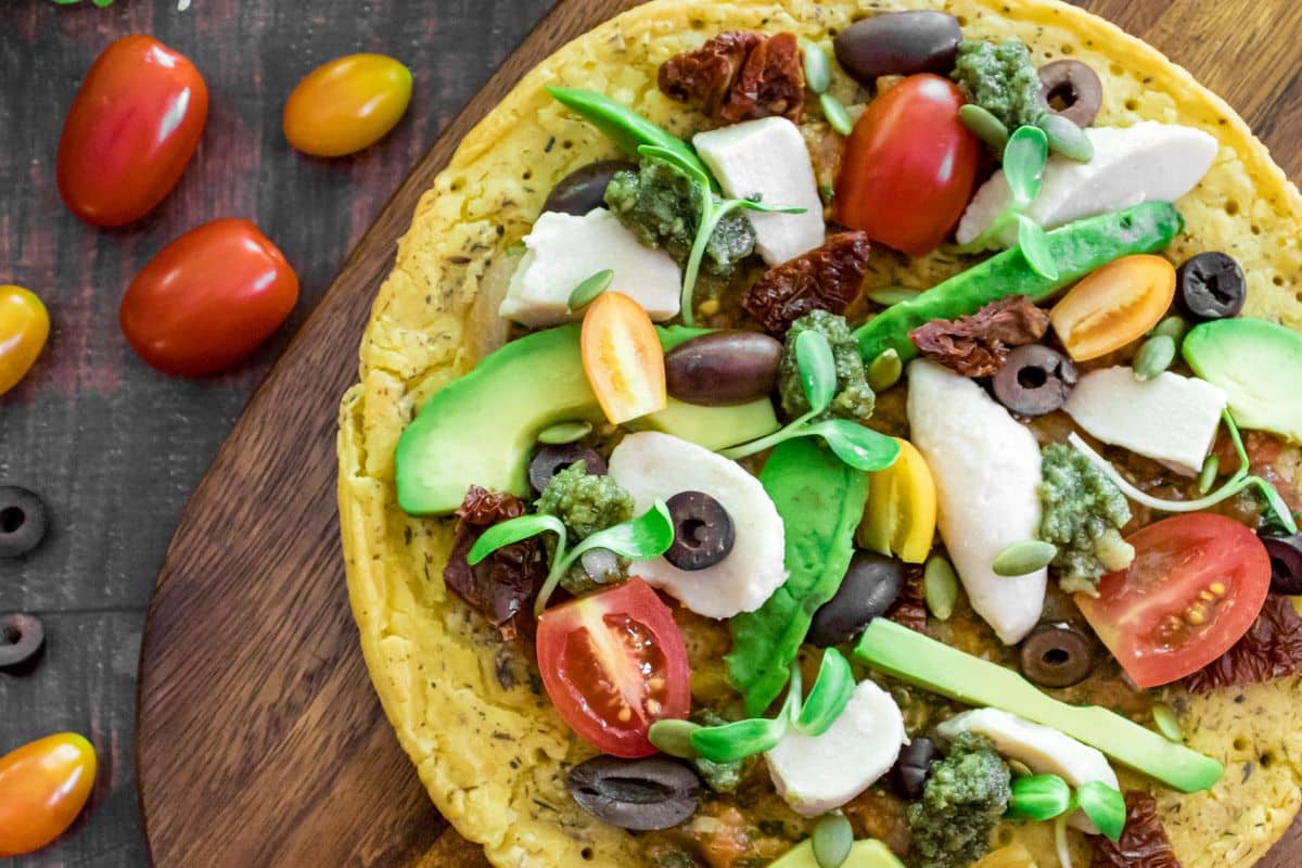 Plant-based chickpea flatbread pizza sliced and topped with fresh rocket, olives and cashew mozzarella