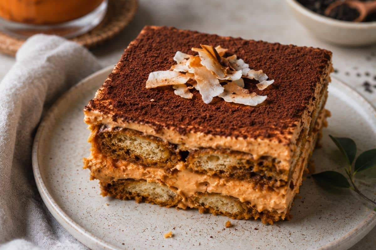 Thai tea tiramisu slice with orange tea cream, cocoa dusting, toasted coconut, and layered sponge