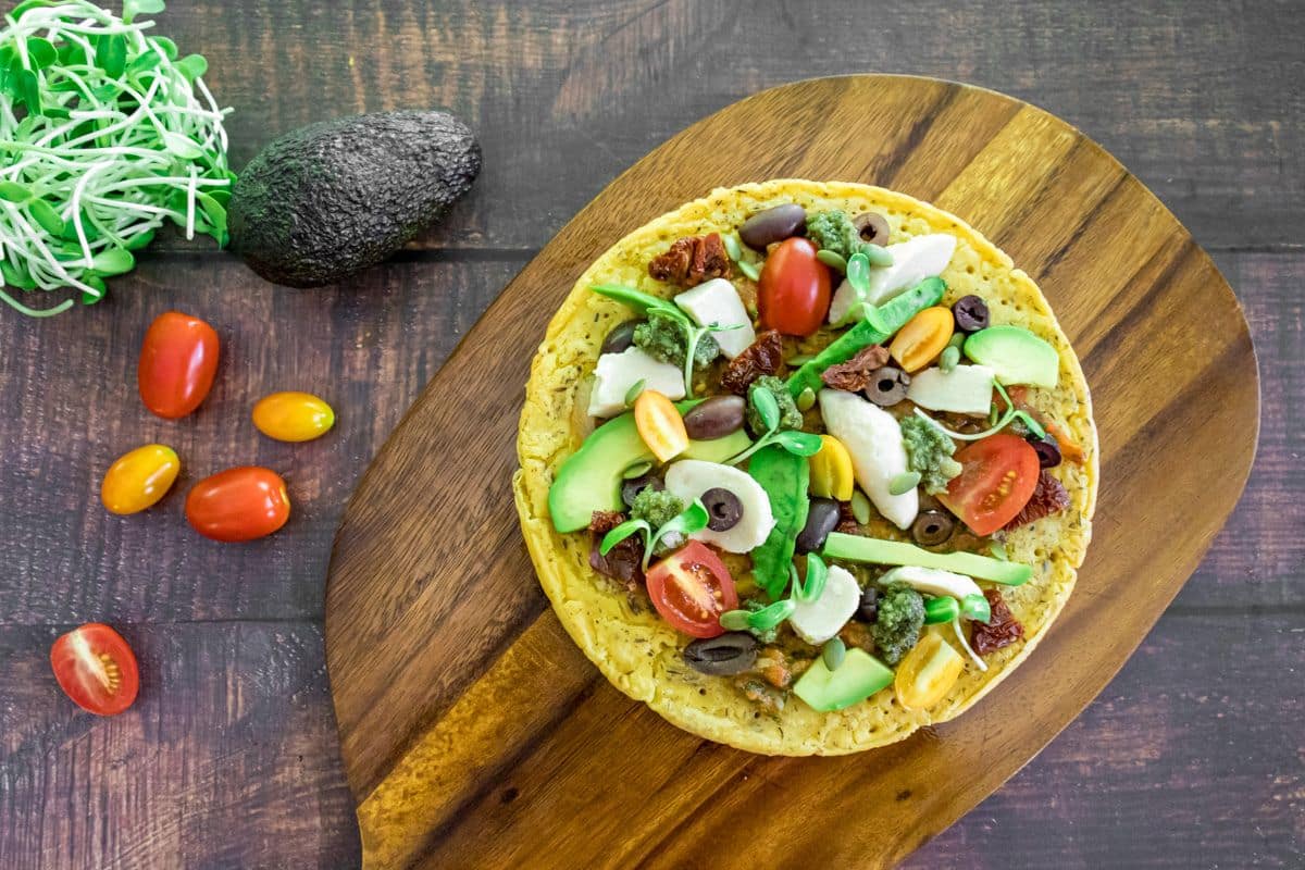 Chickpea flatbread pizza topped with cashew mozzarella, avocado, rocket, olives and sun-dried tomatoes