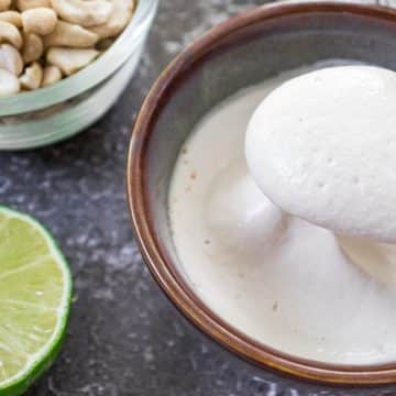Creamy cashew sour cream served in a bowl with fresh lime and cashews