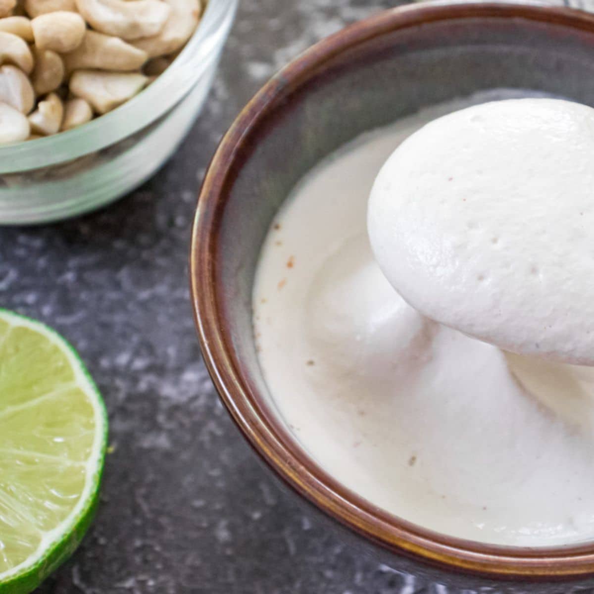 Creamy cashew sour cream served in a bowl with fresh lime and cashews