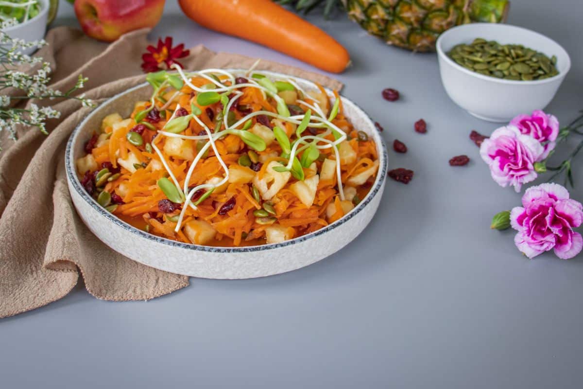 Vegan carrot pineapple salad without mayonnaise, topped with fresh sprouts