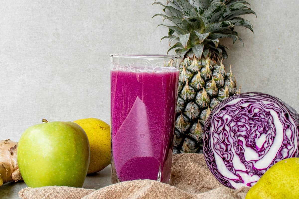 Red cabbage juice served in a glass with fresh pineapple, cucumber, apple, pear and ginger
