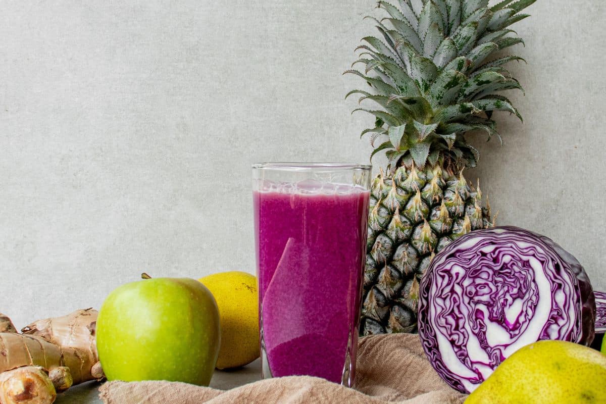 Glass of antioxidant-rich red cabbage juice with fresh purple cabbage and fruit nearby