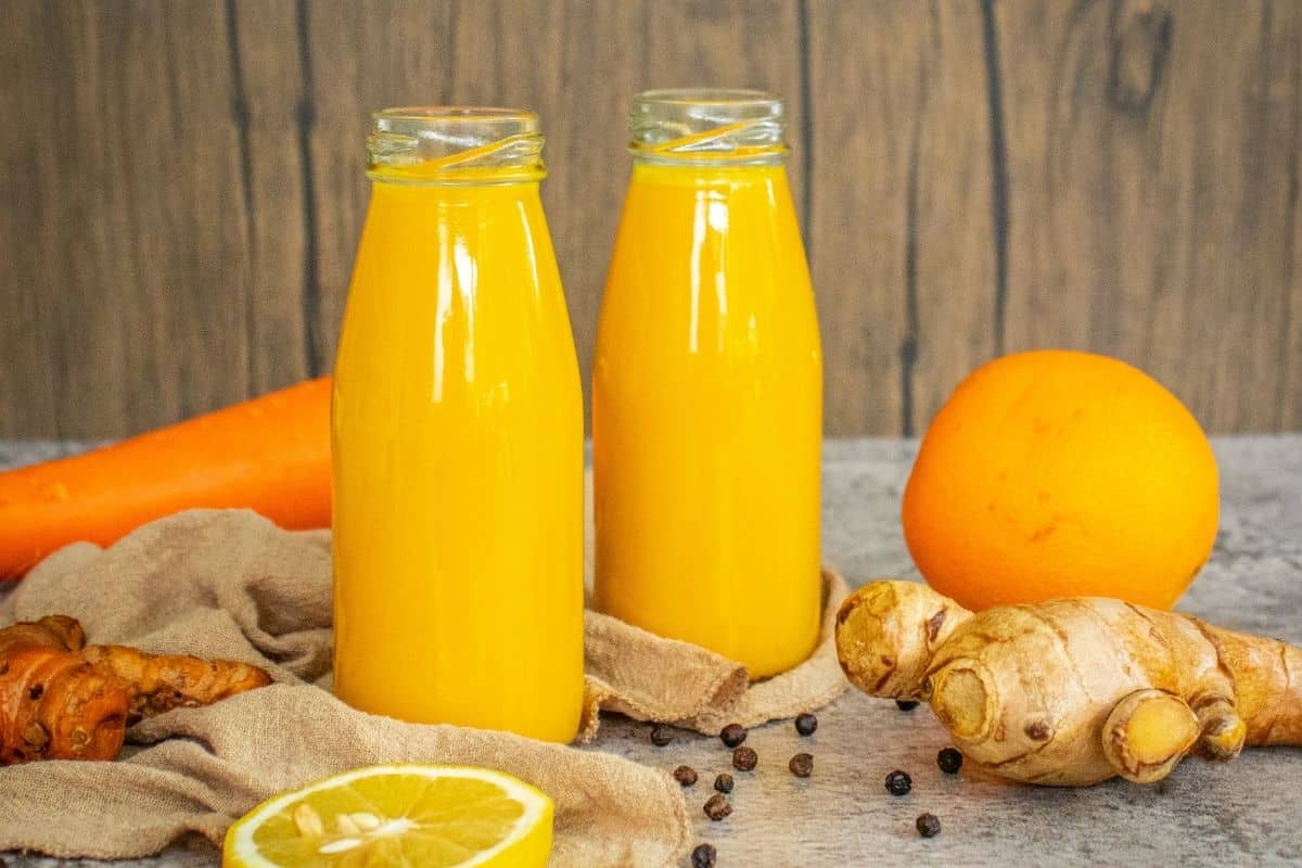 Fresh homemade turmeric shots served in small glass bottles with turmeric root, ginger and citrus.