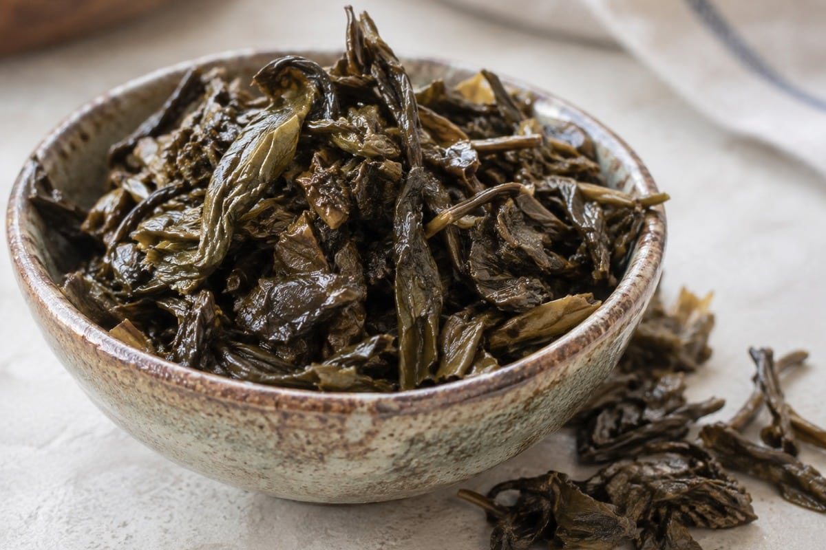 Fermented tea leaves (lahpet) in a rustic ceramic bowl, ready for Burmese Tea Leaf Salad.